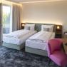 Le Parc Doppelzimmer, © Pia Odorizzi Modernes Hotelzimmer mit zwei Einzelbetten, einem Schreibtisch mit rosa Stuhl und Zugang zu einem Balkon mit Blick ins Grüne.