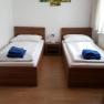 Doppelzimmer, © Haus Nova Zwei Einzelbetten in einem Zimmer mit Wanddekoration und blauen Handtüchern.