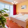 zimmer01, © Hotel Garni Steinfeld Gemütliches Schlafzimmer mit Doppelbett, gelber Wand, rotem Teppich und Pflanzen im Vordergrund.
