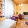 zimmer02, © Hotel Garni Steinfeld Ein gemütliches Einzelzimmer mit Holzboden, einem Bett, einem Schreibtisch mit Stuhl, einem Fernseher und bunten Vorhängen.