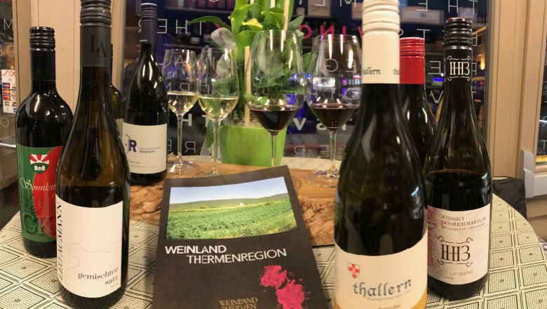 stilvolles Genießen, © Vino Neustadt Weinflaschen und Gläser auf einem Tisch mit einem Prospekt der Weinland Thermenregion.