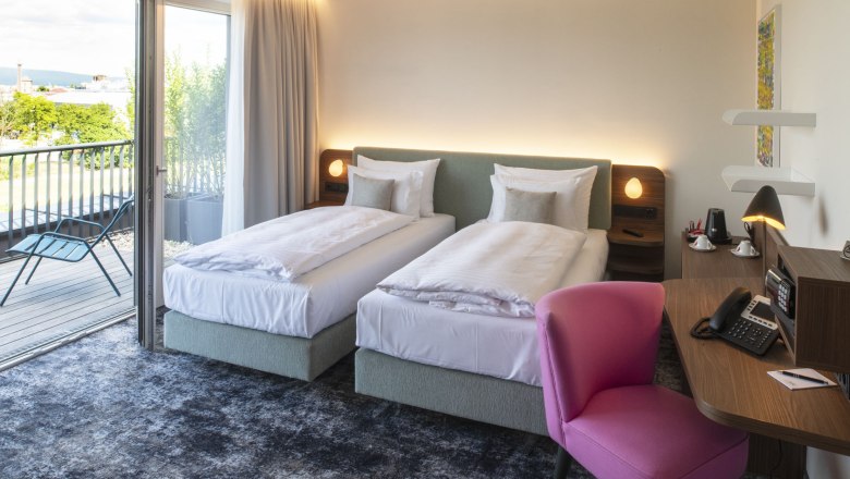 Hotel leParc**** Double room, © Pia Odorizzi Modern hotel room with two single beds, a desk with pink chair and access to a balcony with a view of the greenery.