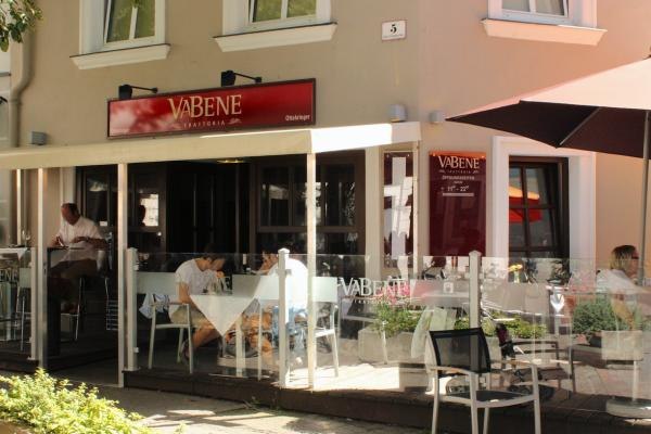 Schanigarten Va Bene, © Koran Außenansicht eines Cafés namens Va Bene mit Schanigarten und Gästen an Tischen.