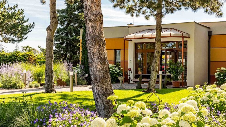 aussen01, © Hotel Garni Steinfeld Eingang eines modernen Gebäudes mit Garten und Bäumen.