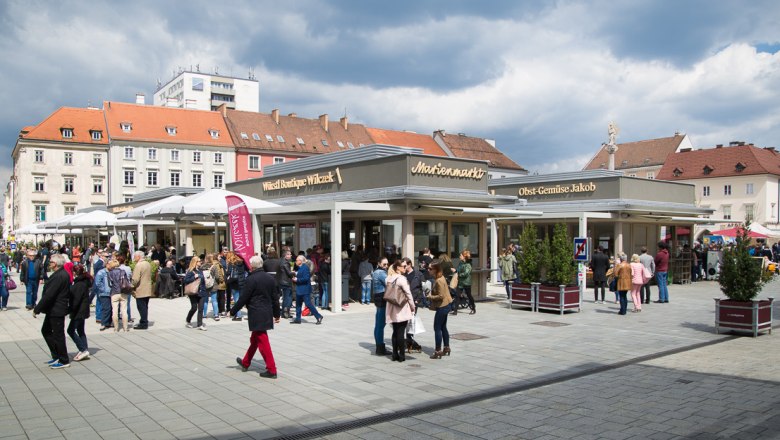 Marienmarkt, © WNSKS Menschenmenge auf einem belebten Marktplatz mit Ständen und Gebäuden im Hintergrund.