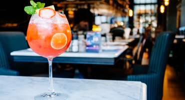 Cocktails, © OX-Fischapark GmbH Ein roter Cocktail mit Limettenscheibe und Minze auf einem Marmortisch in einem stilvollen Restaurant.