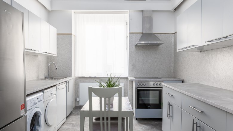 Hotel Zentral guest laundry room and kitchenette, © MartinHaider Fotografie/Hotel Zentral Schwartz GmbH Modern kitchen with washing machine, stove and table with chair.