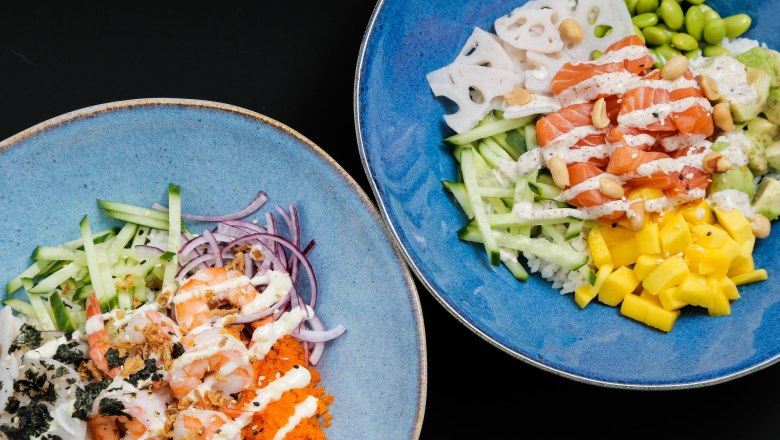 Hawaiianische Bowls, © Ono Zwei blaue Schalen mit hawaiianischen Bowls, gefüllt mit Lachs, Garnelen, Mango, Gurken, Edamame und Soßen.