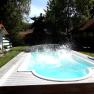Pool, © bed and pool Ein Pool im Garten mit spritzendem Wasser, umgeben von Bäumen und einem kleinen Gebäude mit rotem Dach.