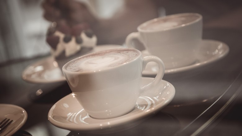 Caféspezialitäten, © Hönigmann/Martin Datzinger Zwei Tassen Kaffee auf Untertassen, im Hintergrund ein Dessert.