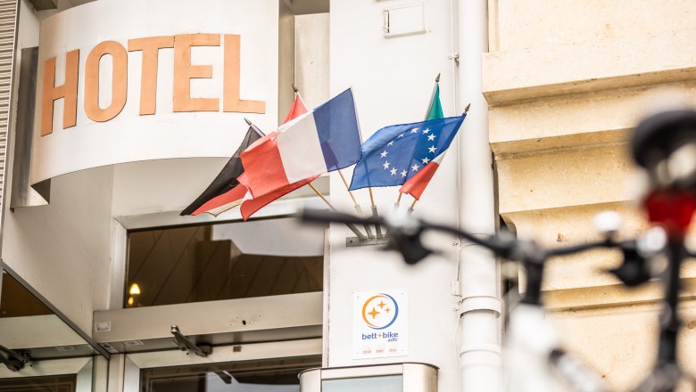 Hotel Central, © Wiener Alpen / Martin Fülöp Entrance of a hotel with several flags and a bicycle in the foreground.