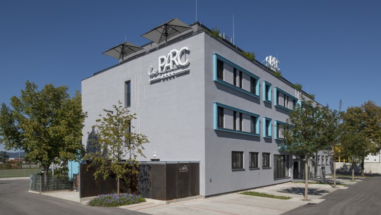 Modernes Gebäude mit der Aufschrift 'Le Parc' und Bäumen im Vordergrund.