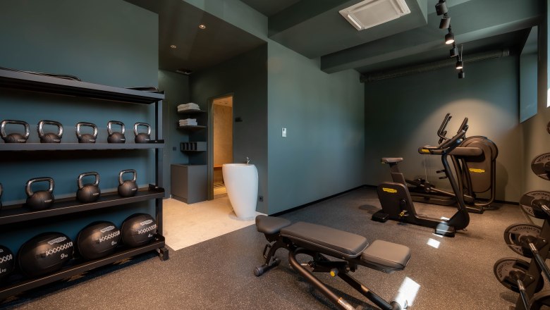 Moderner Fitnessraum mit Kettlebells, Hanteln, Laufband und Ergometer.