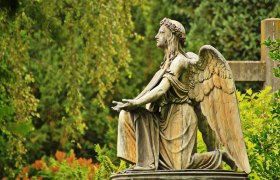 Engelsstatue auf einem Friedhof, umgeben von grüner Vegetation.