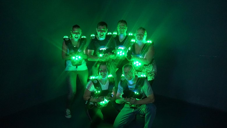 Gruppe von sechs Personen in Lasertag-Ausrüstung mit grünen Lichtern in einem dunklen Raum.