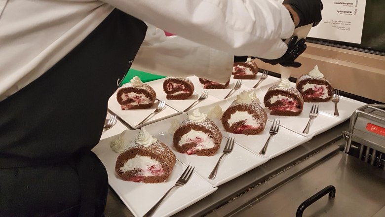 A chef decorates chocolate sponge rolls with cream on white plates.
