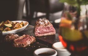 Ein saftiges Steak auf einem heißen Stein, begleitet von Gemüse und Soßen in Schälchen.