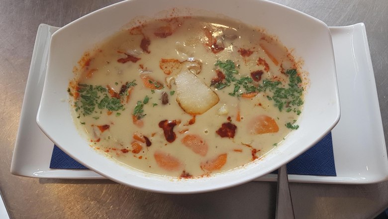 A creamy soup with vegetables and herbs in a white bowl on a plate.