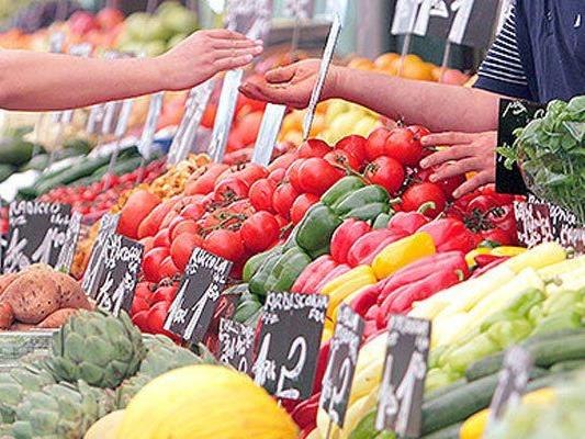 Marktstand mit frischem Gemüse und Obst, Hände beim Bezahlen.