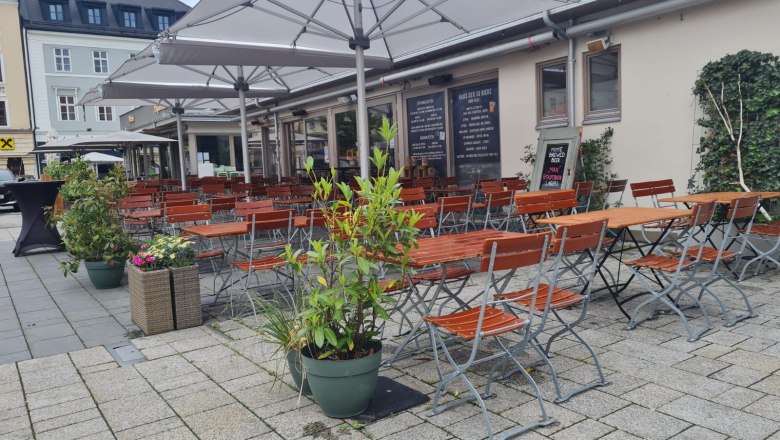 Außenbereich eines Pubs mit leeren Holztischen und -stühlen unter großen Sonnenschirmen.