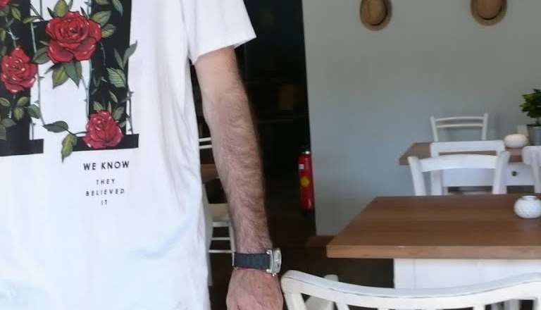 Person in a white T-shirt with a rose motif in a café.