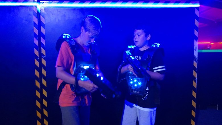 Zwei Jungen in einer Laser-Tag-Arena mit leuchtenden Westen und Laserpistolen.