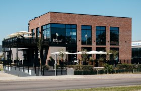 Modernes Backsteingebäude mit großen Fenstern und Terrasse mit Sonnenschirmen.