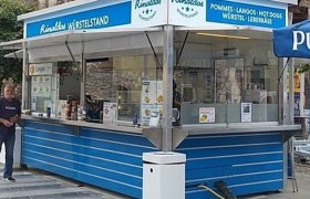 Ein blauer Imbissstand namens Rinaldas W&uuml;rstelstand mit Angeboten wie Pommes und Hot Dogs.