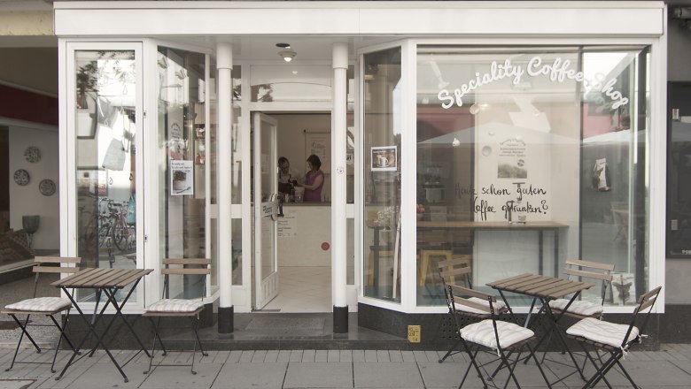 Außenansicht eines Cafés mit Tischen und Stühlen auf dem Gehweg.