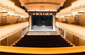 Innenansicht des prachtvollen Stadttheaters Wiener Neustadt mit goldgelben Samtsesseln, Logen und funkelndem Kronleuchter