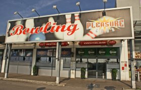 Eingang zu einem Bowlingcenter namens Pleasureland mit gro&szlig;en Schildern und Logos.