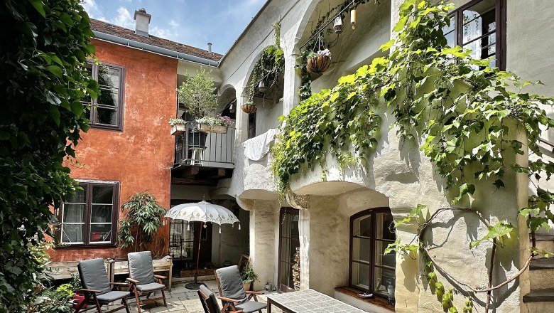 Ein gemütlicher Innenhof mit Pflanzen, Holzmöbeln und einem Sonnenschirm.