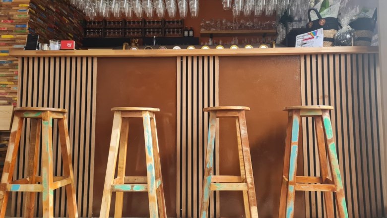 Innenansicht einer Bar mit Holzhockern und Gläsern über der Theke.
