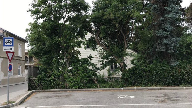 An empty parking lot with a motorhome symbol on the ground, surrounded by trees and a building in the background.