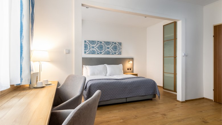 Modernes Hotelzimmer mit Doppelbett, Schreibtisch und Stuhl.