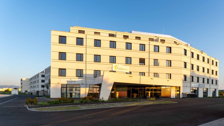 Ein modernes, mehrstöckiges Gebäude mit der Aufschrift 'Plaza INN' bei Sonnenuntergang.