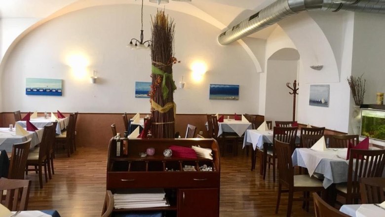 Innenansicht eines Restaurants mit Holzboden, gedeckten Tischen und Wanddekorationen.