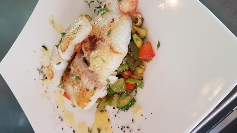 Fried cod on a bed of colorful vegetables, served on a white plate.