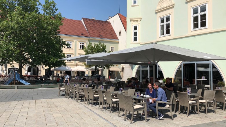 Ein Schanigarten vor dem Eterno mit Sonnenschirmen und Sitzplätzen auf einem gepflasterten Platz.