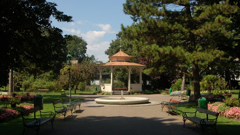 Ein Pavillon im Stadtpark von Wiener Neustadt, umgeben von Bäumen und Blumenbeeten.