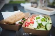Quinoa-Salat mit Gemüse und Brot in Pappschalen serviert.