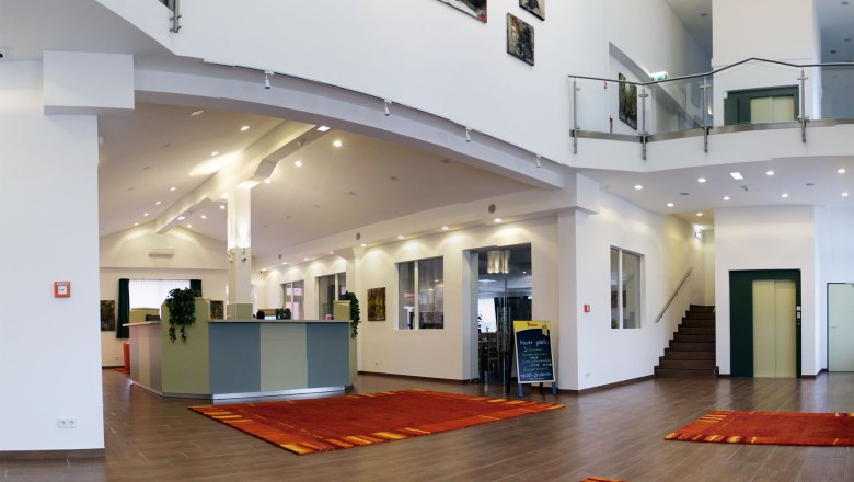 Modern hotel lobby with reception, red carpets and works of art on the walls.