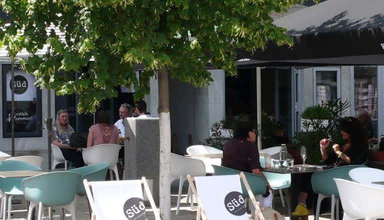 A pavement garden with chairs and deckchairs under a tree.
