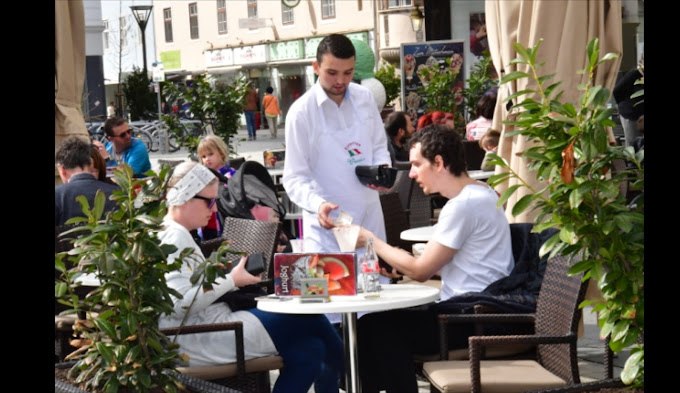 A waiter serves ice cream to a couple on a café terrace.