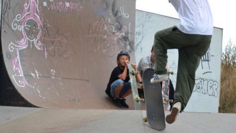 Skateboarder performs trick on halfpipe while two children watch.