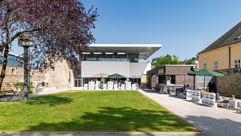 Moderner Garten mit Rasenfläche, Sitzbereich und Gebäuden im Hintergrund.