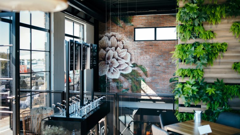 Modernes Café im Obergeschoss mit Pflanzenwand und Blumenmural auf Ziegelwand.