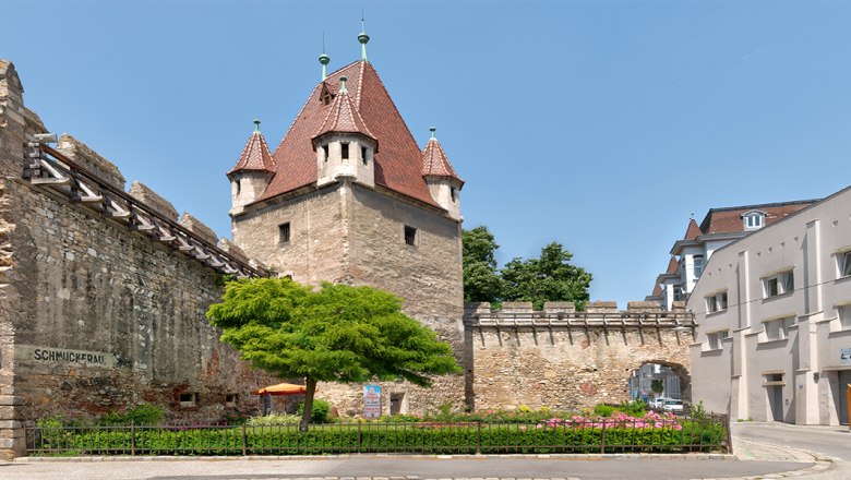 Historic stretching tower with red roof and adjoining city wall in an urban setting.