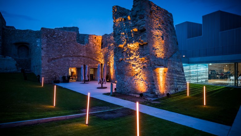 Evening-lit ruins with modern buildings in the background.
