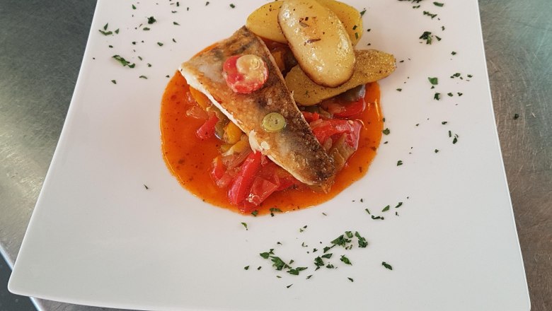 A fish fillet on a white plate, served with paprika vegetables and potatoes, garnished with herbs.